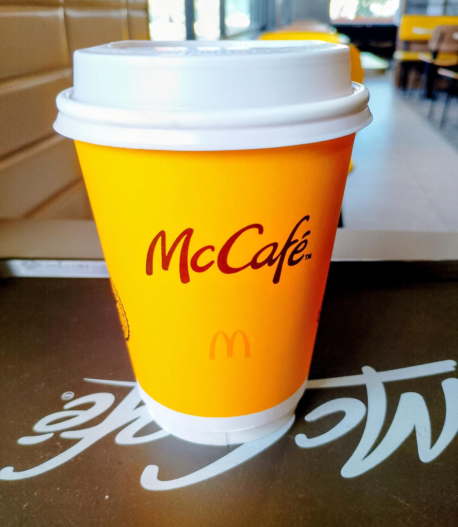 Um copo amarelo com tampa branca da McCafé está sobre uma mesa.