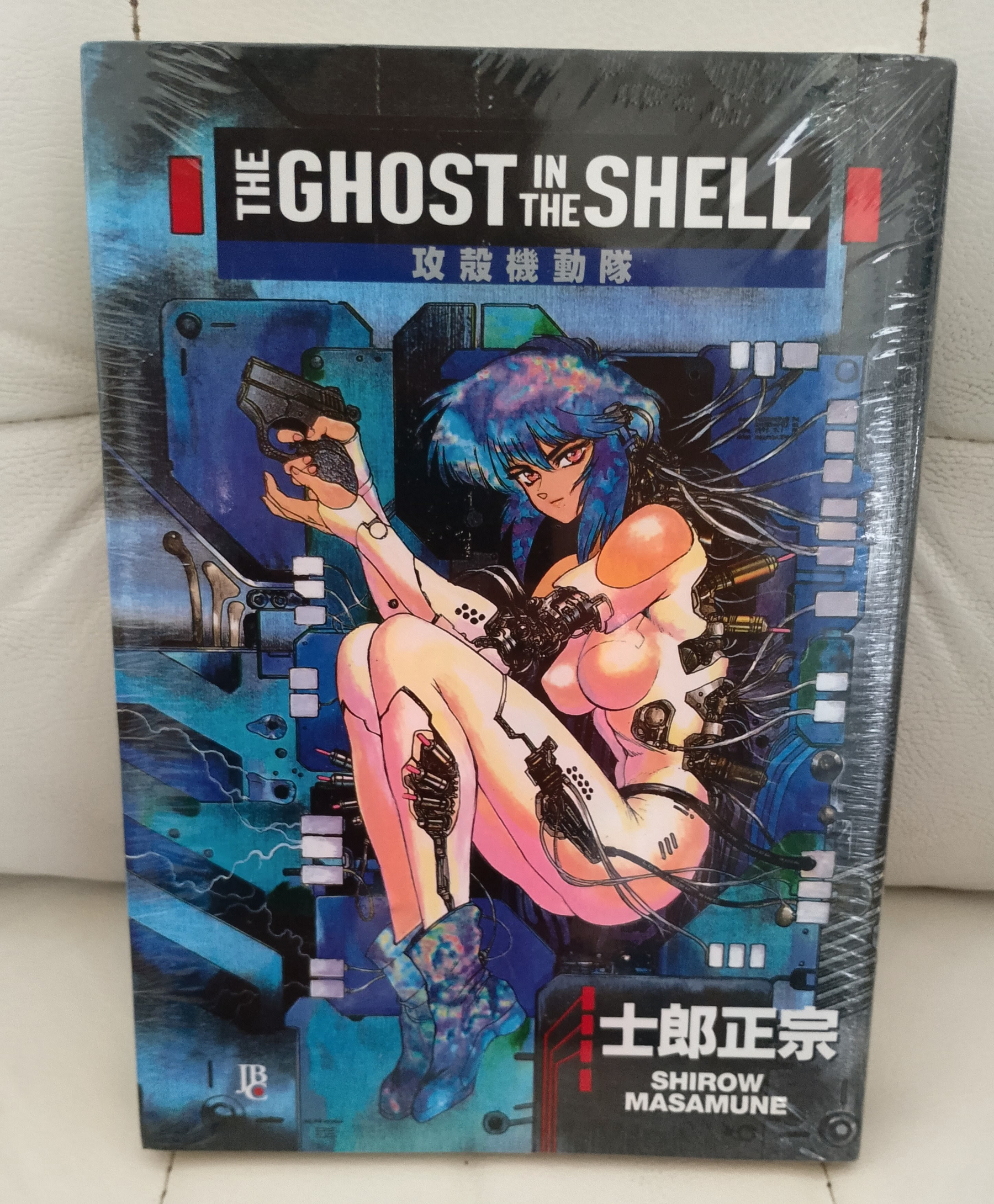 Capa de uma edição de The Ghost in the Shell com uma ilustração de uma figura feminina com cabelo azul e elementos cibernéticos.